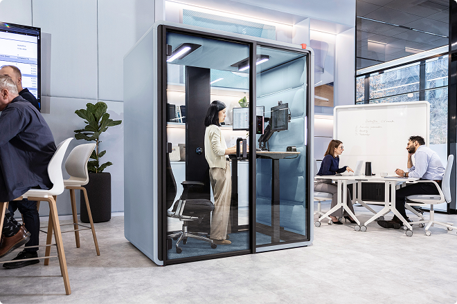 Woman working at the sit-stand desk inside a Hushfree Work pod in an open office